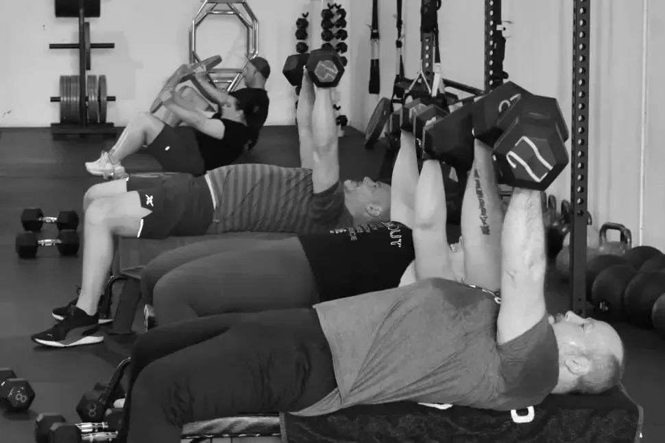 Members pressing dumbbells on benches during a 6 week challenge session