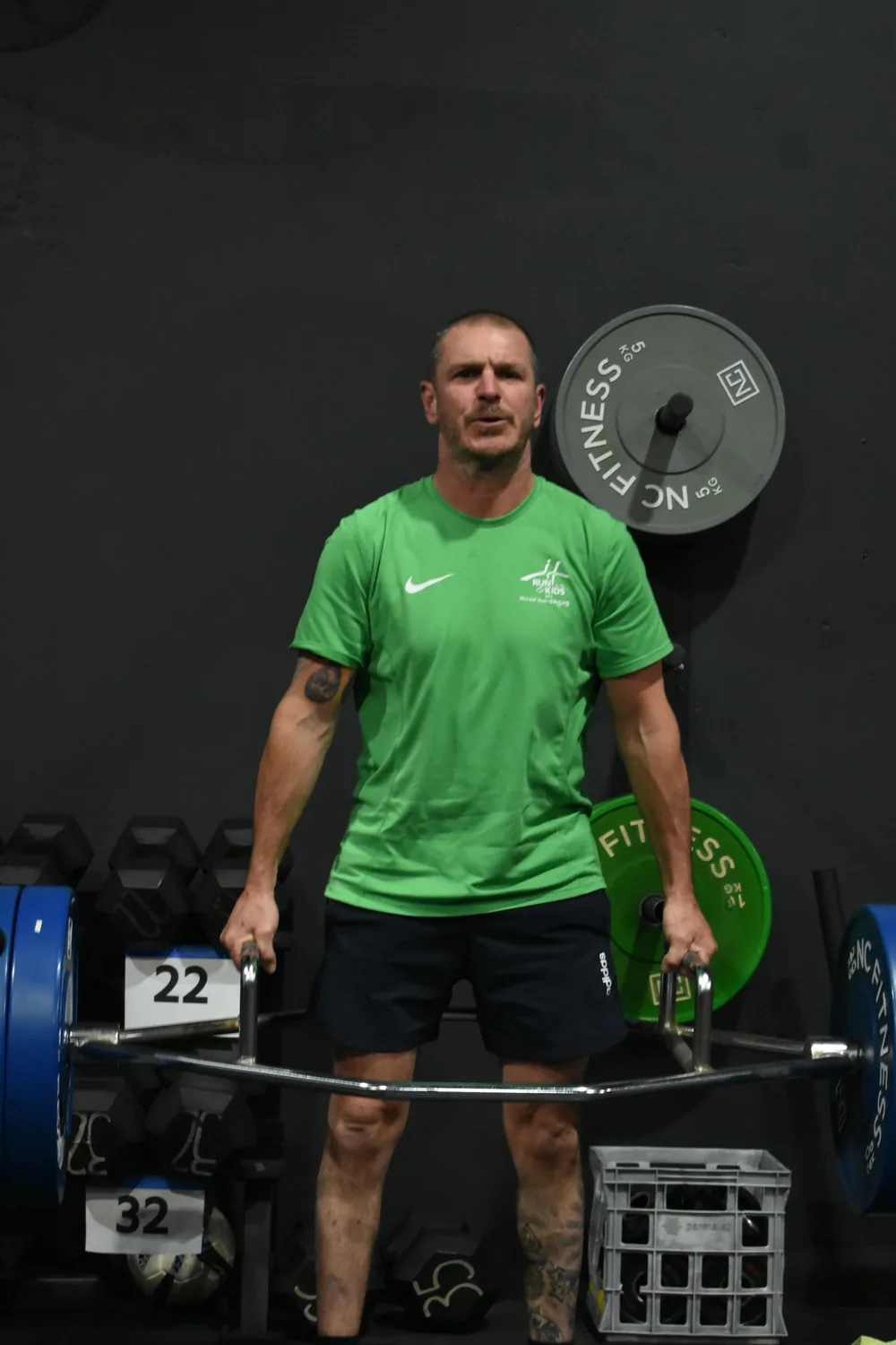 Member lifting a barbell in a green tee during a strength session