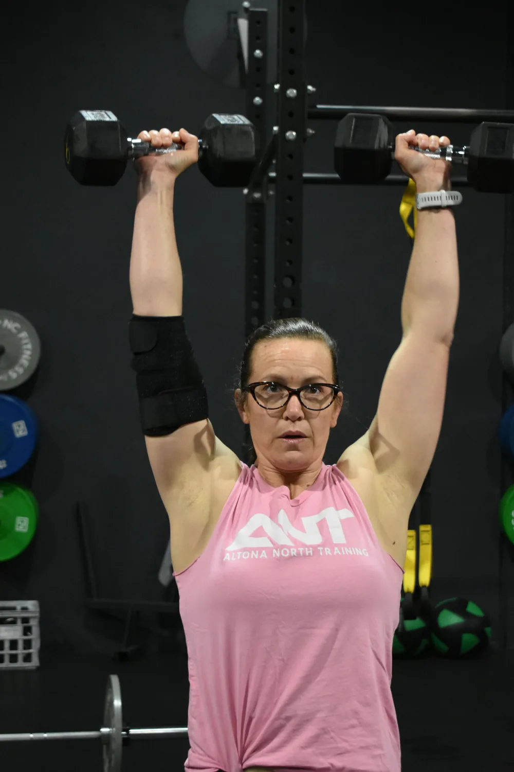 Member pressing dumbbells overhead in an ANT tank top
